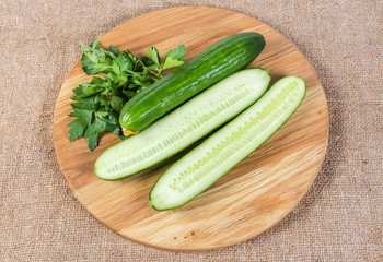 Whole and halves cucumbers and parsley on round cutting board