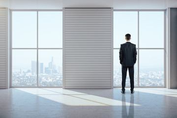 Fototapeta premium Businessman standing in exhibition interior and looking to city.
