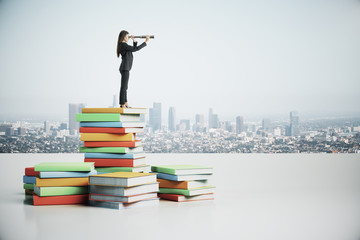 Businesswoman with binoculars standing on book pile.