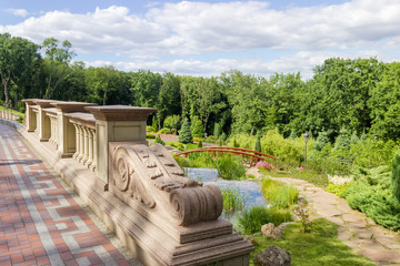 Stone railing on a footbridge over the stream in summer park