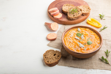 Sweet potato or batata cream soup with sesame seeds in a wooden bowl on a white wooden background. side view, copy space.