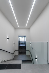 Clean white stairway staircase with glass railing in corridor in office building 