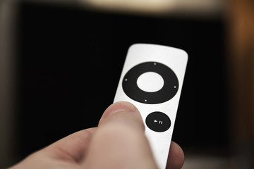 Man presses a button on the modern grey steel remote controll on the background of the TV turned...