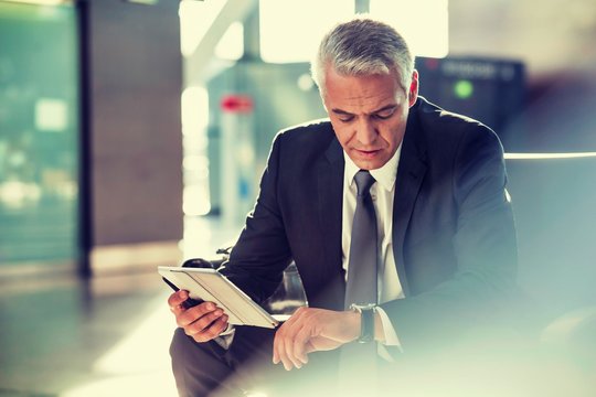 Portrait of mature businessman using digital tablet and checking time while waiting for boarding  - Powered by Adobe