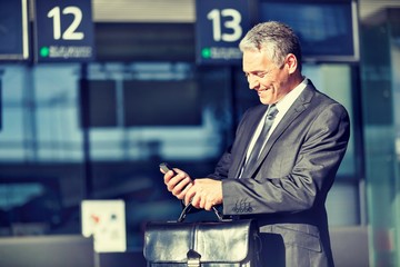 Portrait of mature businessman smiling and using smartphone while waiting for boarding