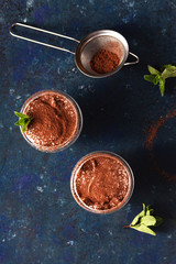 Tiramisu in a transparent with cocoa and mint on a blue dark background. Top view, flat lay, copy space.