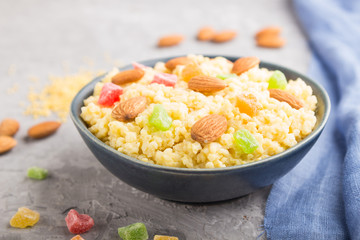 Millet porridge with candied fruits and almonds in blue ceramic bowl on a gray concrete background. Side view, selective focus.