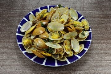 Traditional stir fried clams with curry powder and green basil on the plate. Famous hot plate in Asia restaurant. Delicious seafood appetizer menu in party.