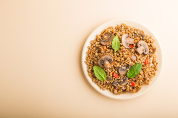 Spelt (dinkel wheat) porridge with vegetables and mushrooms on ceramic plate on orange background. Top view, copy space.