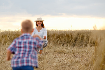 Naklejka na ściany i meble Happy mother and son are running through a wheat field in summer