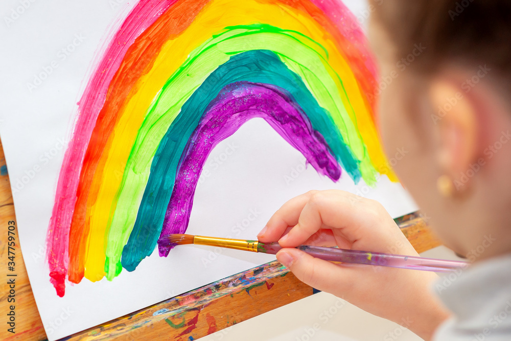 Wall mural Child is drawing rainbow with watercolors on the sheet of paper on the easel. Creativity concept.