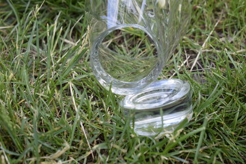 Broken glass cup on the green grass in the garden. Broken thick bottom of the glass.