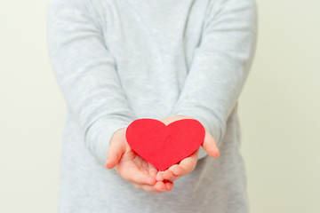 Closeup of hands of child holding red paper heart on white background. Red heart in child's hands.