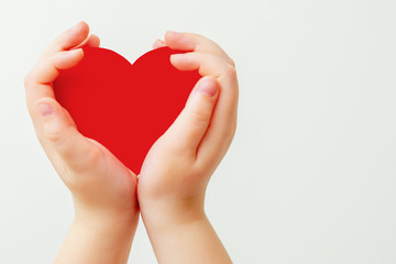 Closeup of child's hands holding paper red heart on white background. Concept of love.