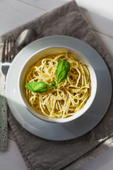 Pesto pasta in a white bowl on a light background with sunlight