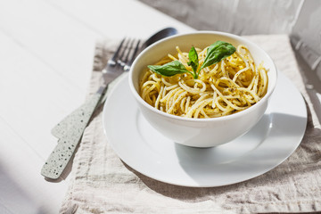 Pesto pasta in a white bowl on a light background with sunlight