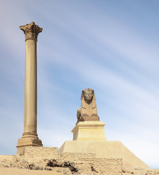 The famous Pompey pillar with a sphinx in the Upper Egyptian city of Alexandria. A popular travel destination. It is day and blue sky. A nice long exposure with moving clouds.