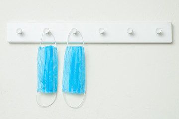 Protective medical masks hanging on hooks of wooden white hanger on a white wall at home. Stay Home concept.