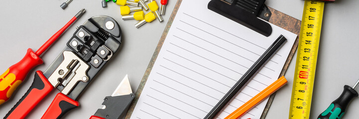 Open Notepad and tools of an electrician-installer or Builder on a gray background. Concept of drawing up an estimate or list of construction materials for installation works. Banner