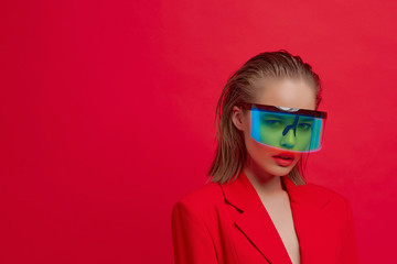 A cool stylish girl with a fashionable hairstyle and stylish glasses with a large glass poses on a bright red background