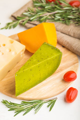 Green basil cheese and various types of cheese with rosemary and tomatoes on wooden board on a white wooden background. Side view, close up.