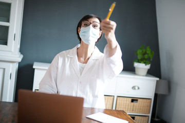 Frau arbeitet in Arztkittel und Mundschutz im Homeoffice oder Praxis zuhause.	
