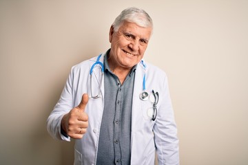 Senior handsome hoary doctor man wearing coat and stethoscope over white background doing happy...