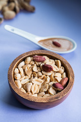 Peanuts in a wooden bowl and spoon with peanut butter on blue background. Healthy snack. Vertical picture.