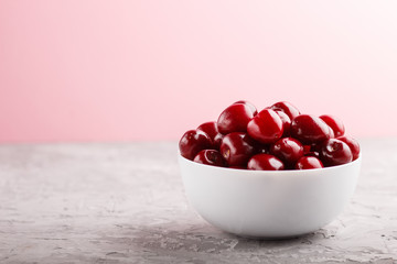 Fresh red sweet cherry in white bowl on gray and pink background. side view.