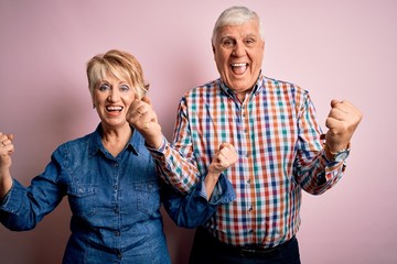 Senior beautiful couple standing together over isolated pink background celebrating surprised and amazed for success with arms raised and open eyes. Winner concept.