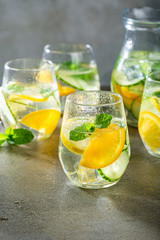 Summer healthy lemonade, cocktails of citrus infused water or mojitos, with lime lemon orange, ice and mint, diet detox beverages, in glasses on gray background.