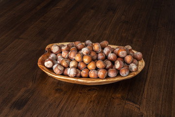 nuts in a wooden plate on a wooden table top of boards with a dark textured surface.