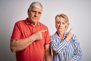 Senior beautiful couple standing together over isolated white background Pointing with hand finger to the side showing advertisement, serious and calm face