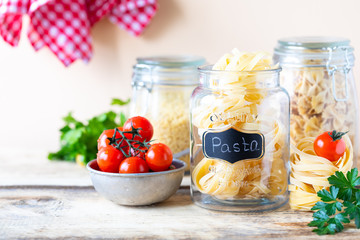 Different types of italian pasta in glass jars on a yellow wooden table. Diet and nutrition concept.