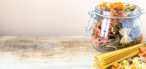 Different types of italian pasta in glass jars on a yellow wooden table. copy space