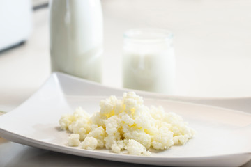 Milk kefir grains in plate with a glass of kefir in the back, photographed with natural light