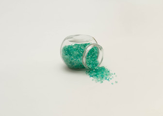 Jar with turquoise is on the centre of the frame. Horizontal photo. Object on a white background. Bank is lie on its side. Bath salt spilled out into the background. Copyspace for text.