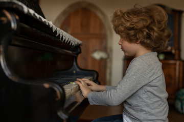 Little boy plays on grand piano at home. Young musician.