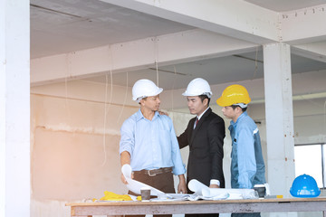 Businessman engineer and worker looking paper plans at construction site.