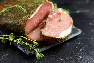Gerky pork with spices, fresh green thyme, slate cutting board on black stone table. Polendwitz is a jerky tenderloin