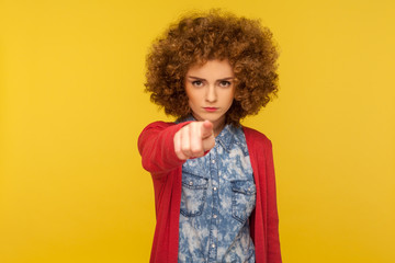 Hey you! Portrait of serious aggressive woman with curly hair in casual outfit pointing to camera, noticing and indicating finger, choosing guilty. indoor studio shot isolated on yellow background