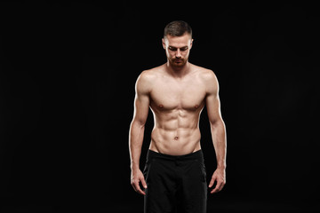 Fototapeta na wymiar Strong athletic man - crossfit athlete fitness model showing his perfect body isolated on black background with copyspace. Ectomorph bodybuilder with perfect abs, shoulders, biceps, triceps and chest.