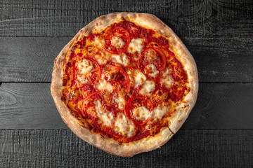 Tasty hot italian pizza with tomatoes and mozzarella on black wooden table. Pizzeria menu. Concept poster for Restaurants or pizzerias