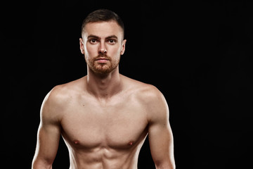 Fototapeta premium Strong athletic man - crossfit athlete fitness model showing his perfect body isolated on black background with copyspace. Ectomorph bodybuilder with perfect abs, shoulders, biceps and chest. Close-up