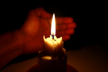 Candle in the dark with a hand covering it from the wind