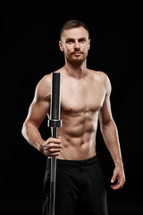 Fototapeta na wymiar Strong athletic man - crossfit athlete fitness model showing his perfect body isolated on black background with copyspace. Holds a sports bar next to him, close-up, perfect abs, shoulders and chest