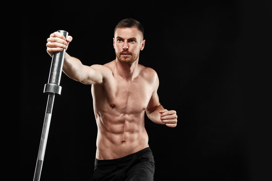 Strong athletic man - crossfit athlete fitness model showing his perfect body isolated on black background with copyspace. Doing an exercise with a barbell, close-up, perfect abs, shoulders and chest