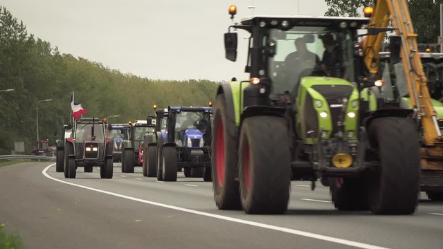 Parade of tractors driving side by side on highway causing slow traffic jam in protest of new policies