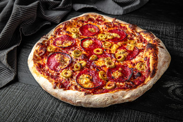 Tasty hot italian pizza with pepperoni and olives on black wooden table. Pizzeria menu. Concept poster for Restaurants or pizzerias