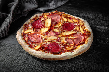 Tasty hot italian pizza with ham, pepperoni and potato chips on black wooden table. Pizzeria menu. Concept poster for Restaurants or pizzerias